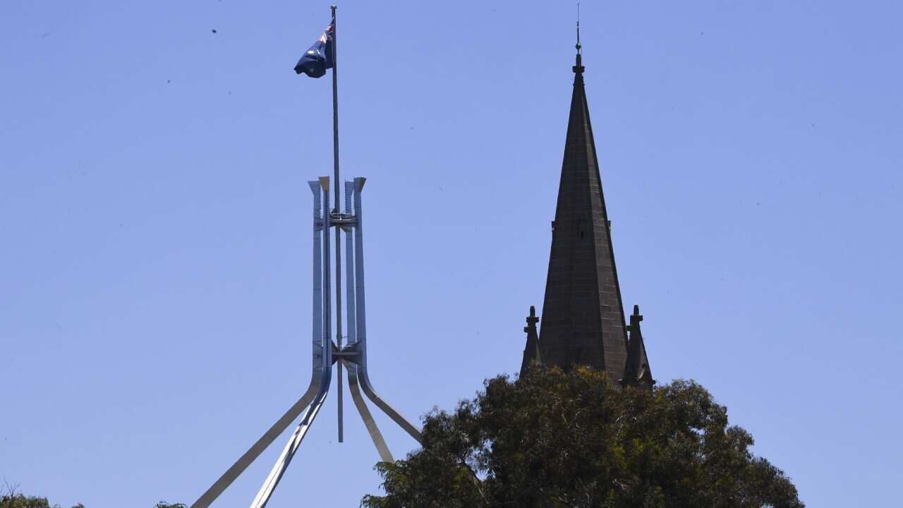 The tower of St Andrews Presbyterian Church is seen near the flag pole of the Australian Parliament House in Canberra, Tuesday, December 21, 2021. (AAP Image/Lukas Coch) NO ARCHIVING