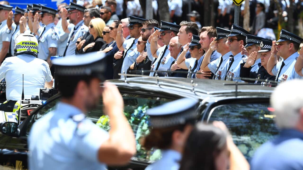A procession is seen following a memorial service, with police officers lining the road.