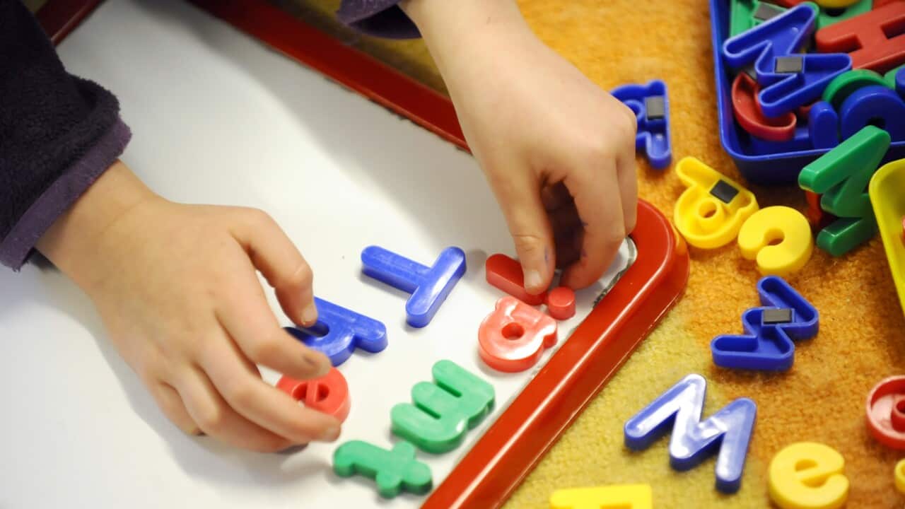 Close-up of a child's hands playing with colourful letters on a magnetic board