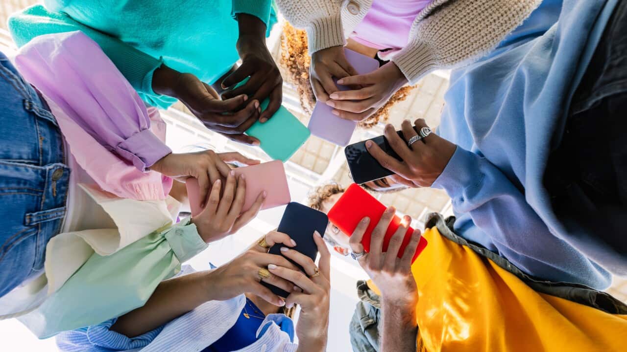 Low angle view of young group of people holding cellphone devices at city street. Diverse addicted teen friends watching social media content on smartphone app. Youth, gen tech people and technology lifestyle concept.