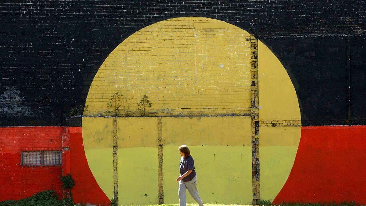 A person walks in front of a mural of the Aboriginal flag.