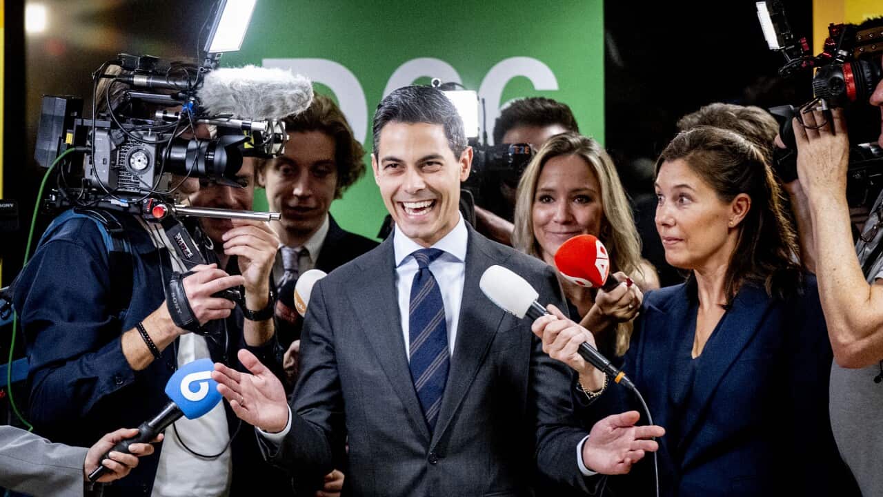 A man wearing a suit and smiling while being interviewed in front of TV cameras