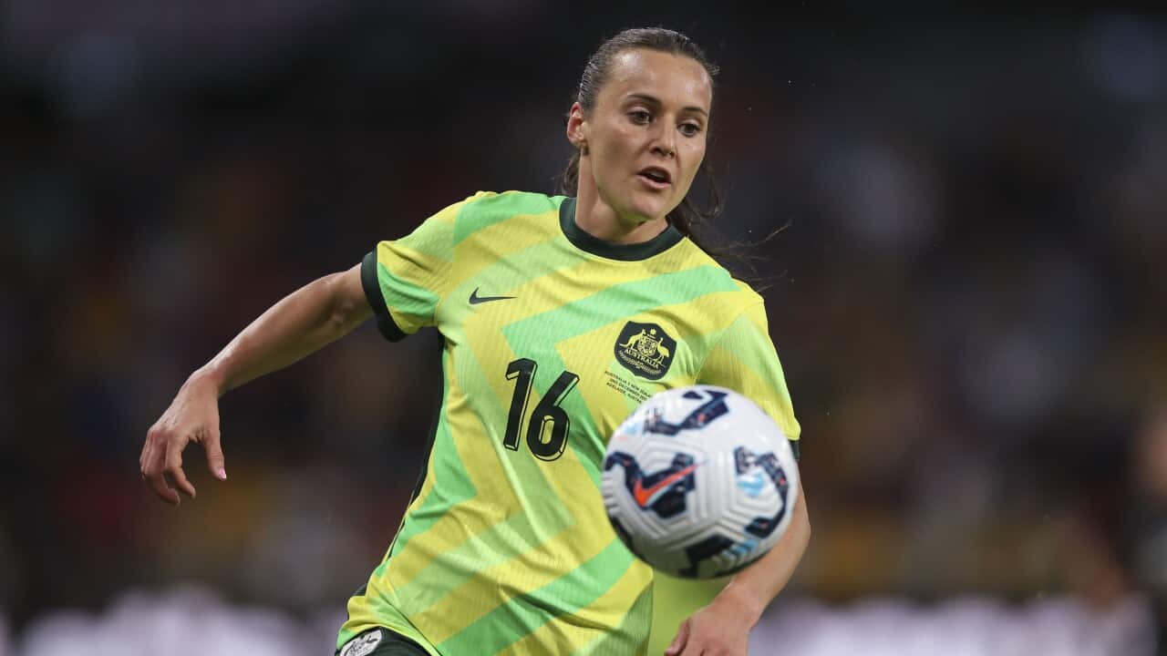 A women in a yellow and green football shirt running behind a football