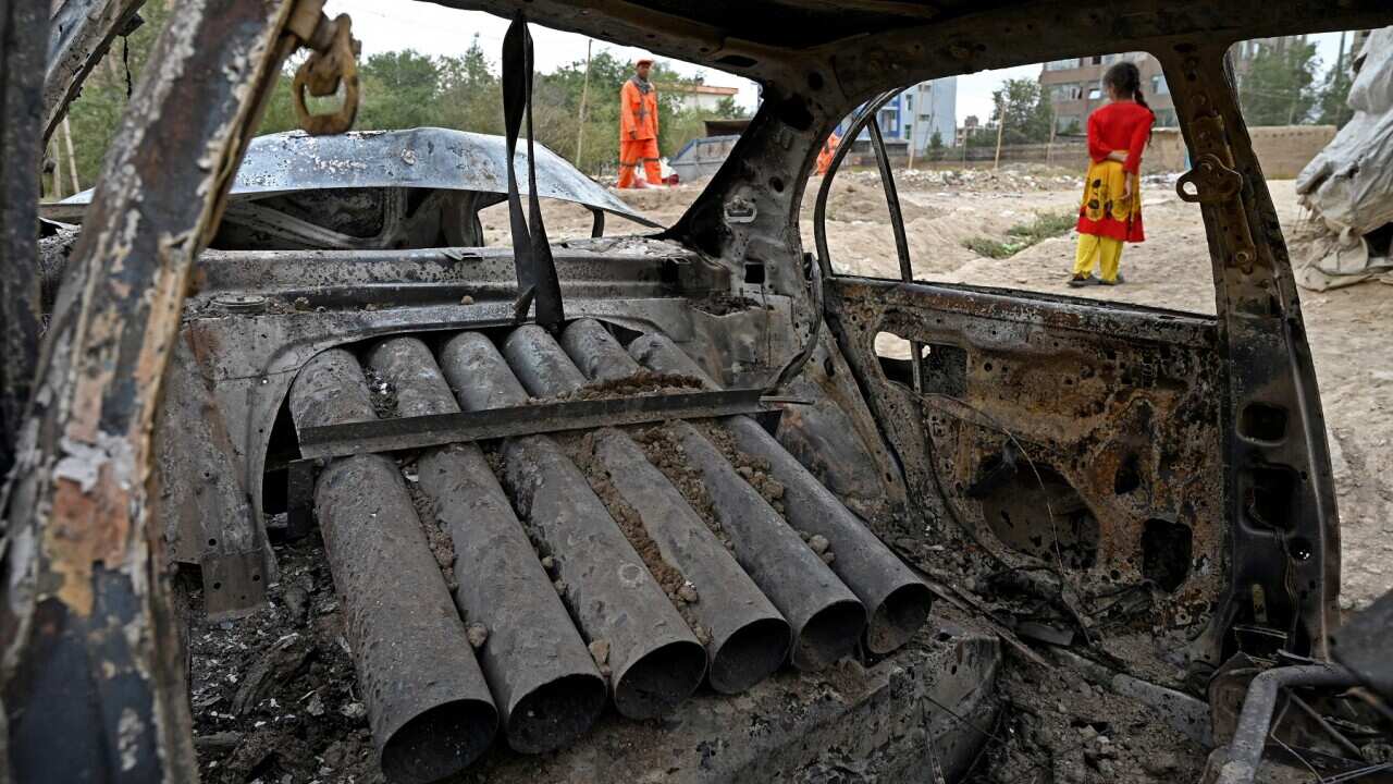 A girl stands next to a damaged car in Kabul