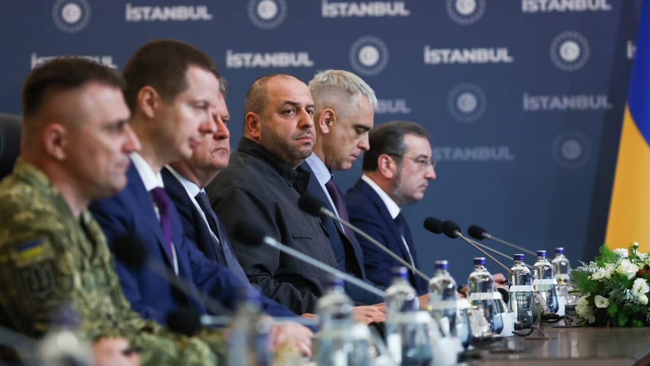 Six men sitting at a table in front of microphones