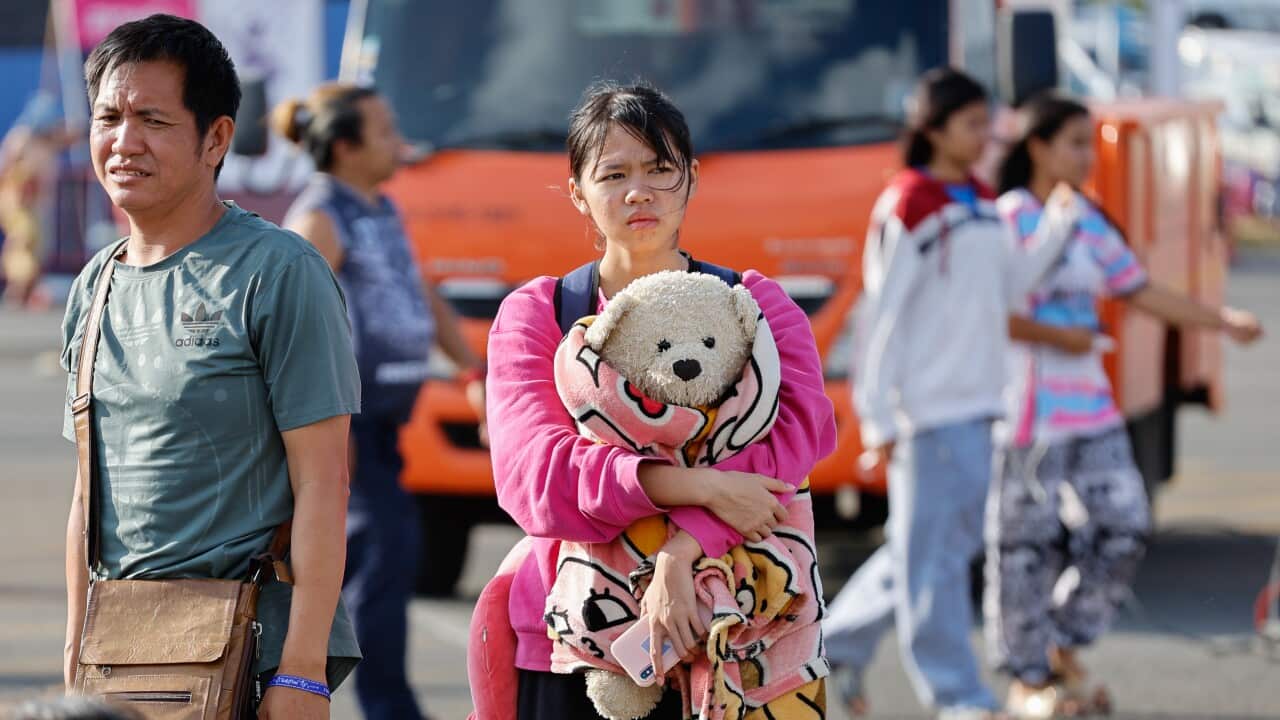 A girl holding a large teddy bear standing outside, next to a man in a green t-shirt.