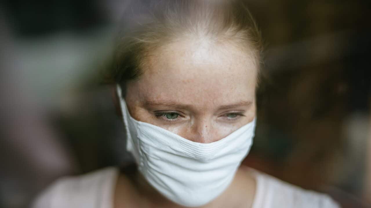 Woman with mask behind window.