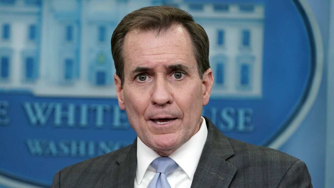 A man in a suits points while standing in front of the White House logo