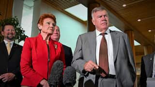 Pauline Hanson stands next to David Farley as they speak in front of microphones.