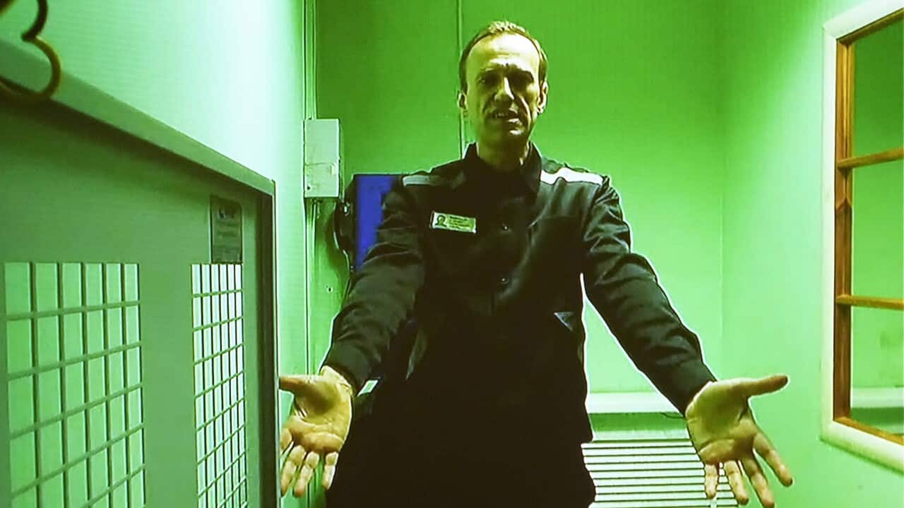 A middle aged man in a prison jumpsuit appears on a green-tinted television screen.