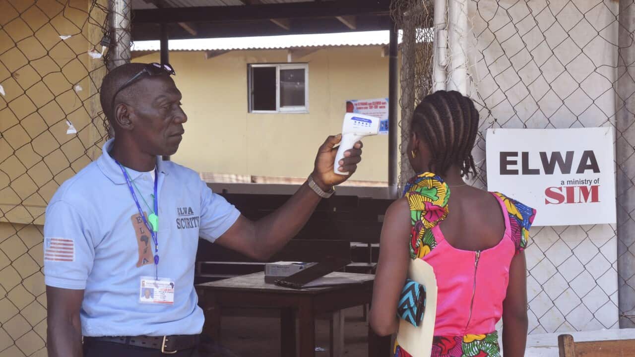 A unidentified family member, right, of a 10-year old boy that contracted Ebola, has her temperature measured by a health worker before entering the Ebola clinic