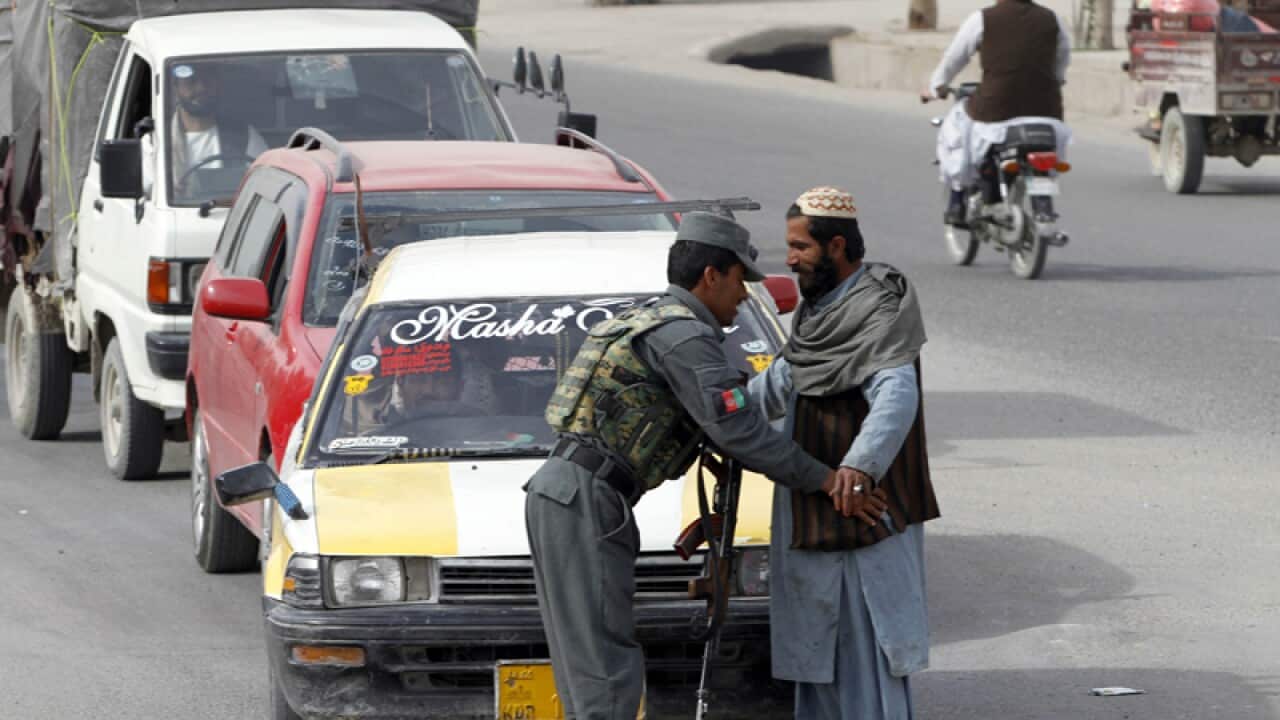An Afghan policeman searches a passenger at a checkpoint in Kandahar