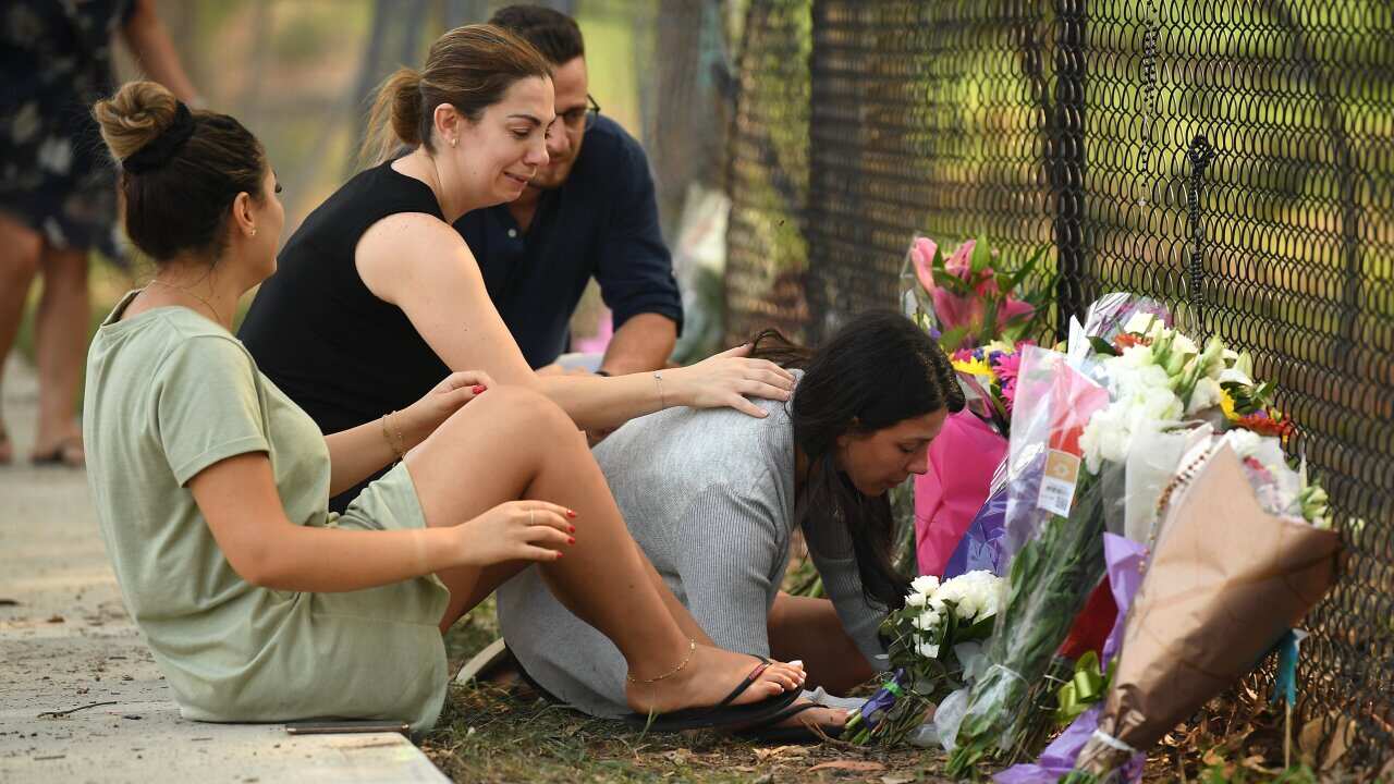 A group pauses near flowers placed at the scene where seven children were hit by a four-wheel drive in the Sydney suburb of Oatlands.