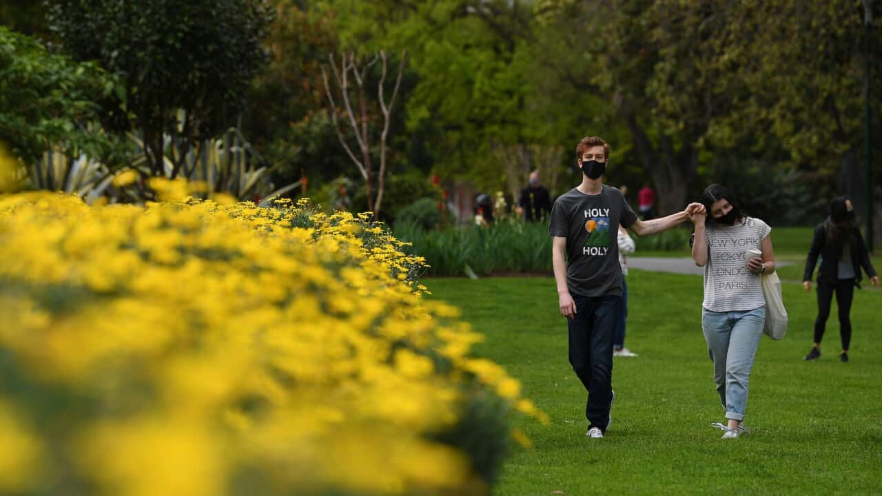 People wearing face masks hold hands while walking through Carlton Gardens in Melbourne, Saturday, September 11, 2021. Victoria has recorded 450 new locally-acquired COVID-19 cases in the past 24 hours. (AAP Image/James Ross) NO ARCHIVING