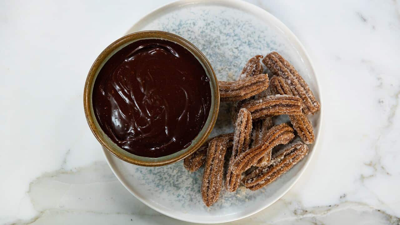 A bowl of glossy chocolate sauce sits on a wide, speckled plate. Beside the bowl, on the plate, sit a pile of ridged long, brown pastry strips.