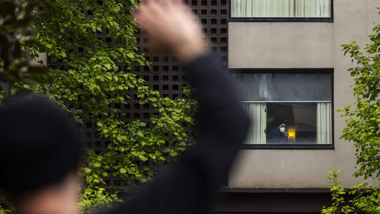 A person looks out a window of the Park Hotel in Carlton as a refugee advocate (left) waves.