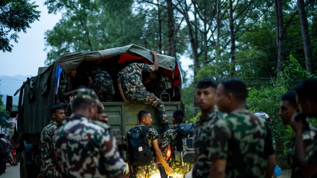 Soldiers in green military fatigues around a military truck, some people are inside in the back of it