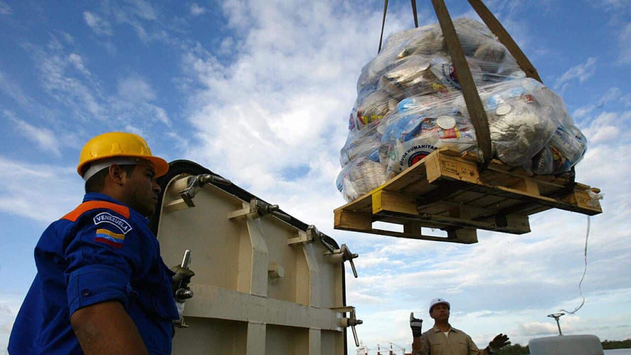 A member of Venezuela's Civil Protection and another worker, unload packages of food aid.