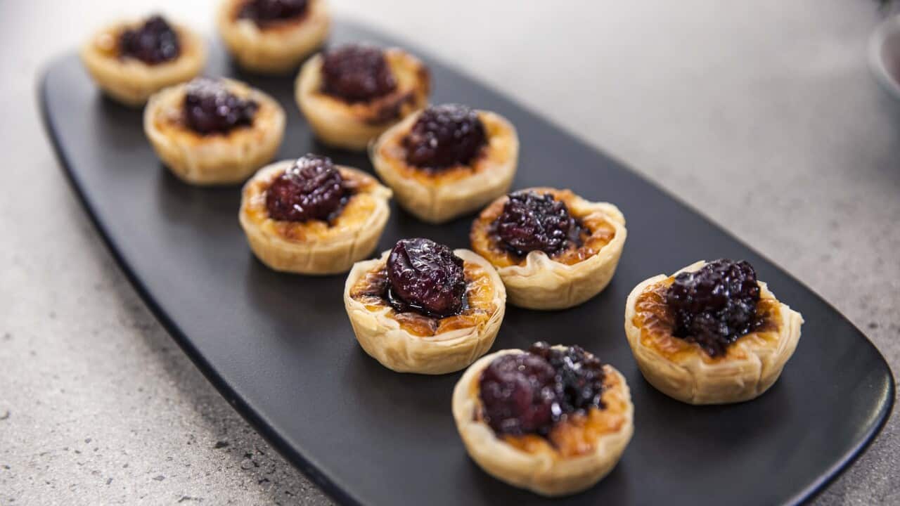 Ten small tartlets sit on a long platter, each topped with a grape relish.