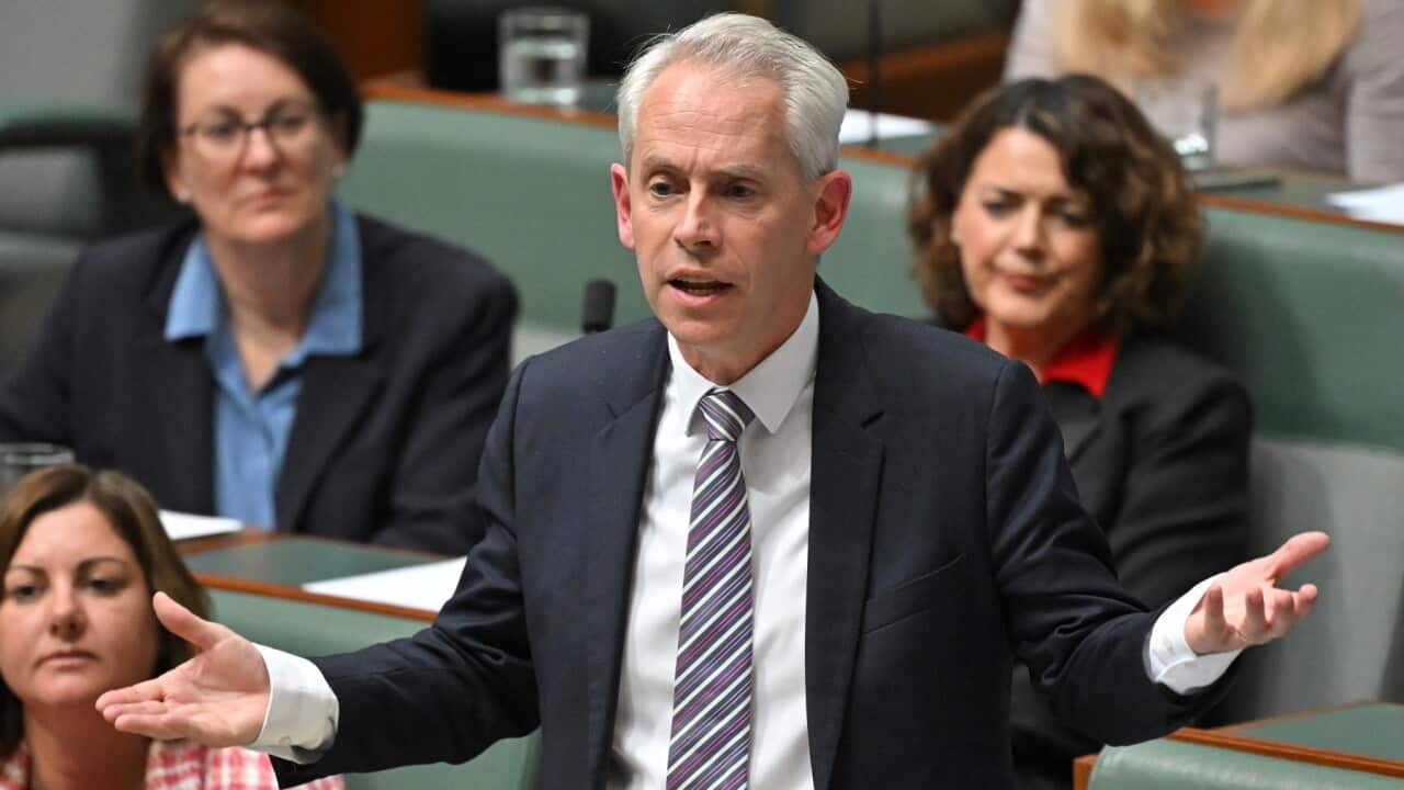 A man in a black suit standing up in front of green benches