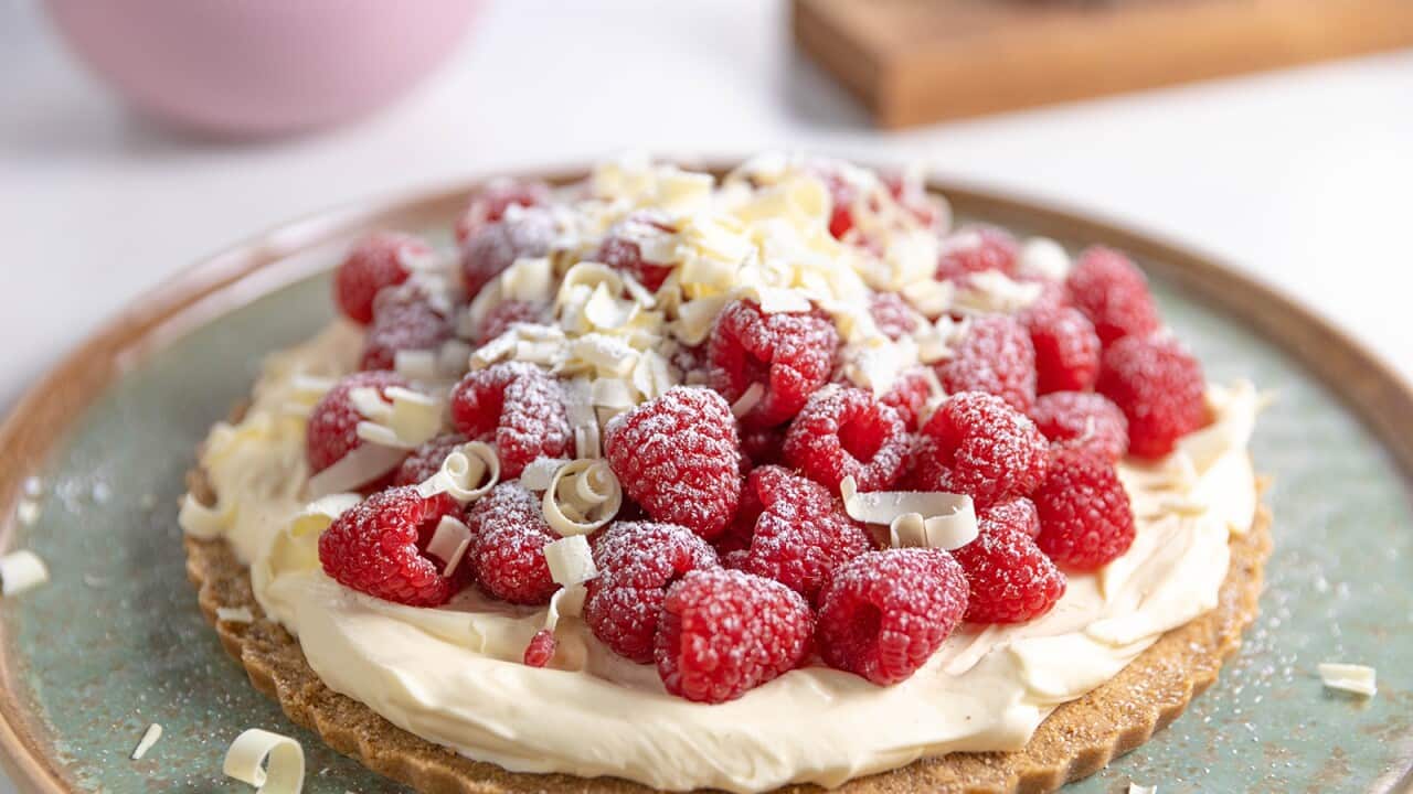 On a lovely wide, flat green-toned plate sits a disk of pastry, topped with a layer of whipped cream, fresh raspberries and white chocolate shavings.