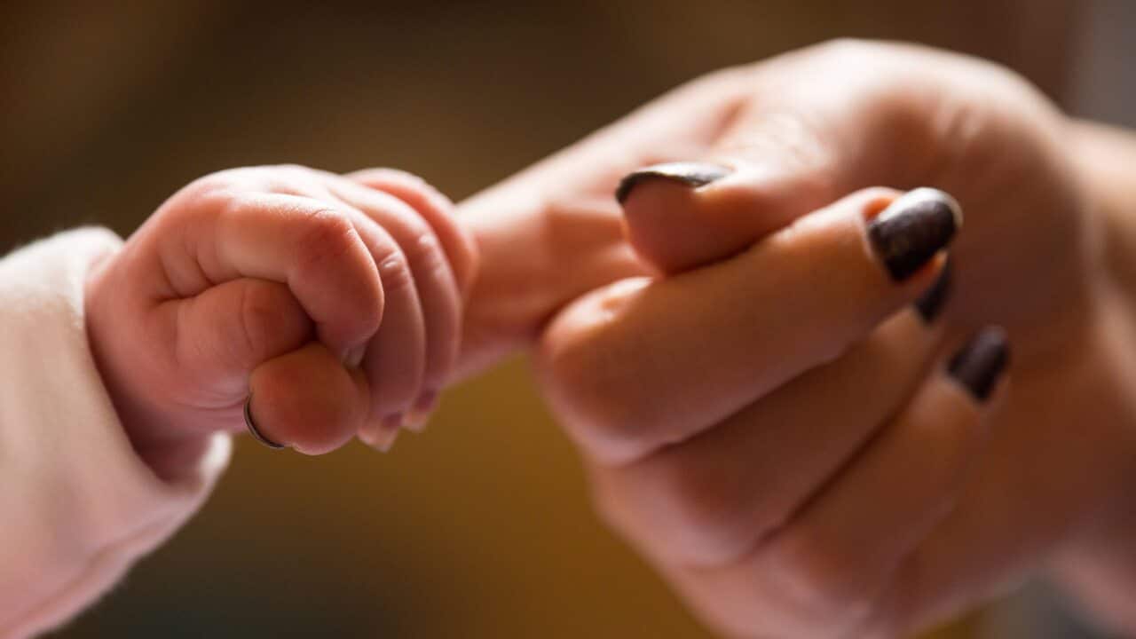A baby holding the finger of its mother