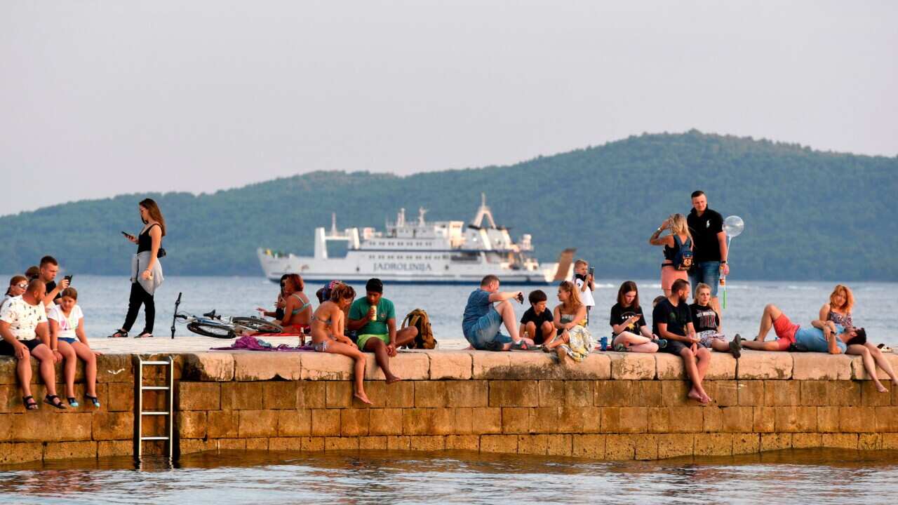 Tourists sit or walk on a pier at sunset in Zadar, on the Adriatic coast on August 6, 2020. - A large number of tourists visited the Zadar Riviera, regardless of the novel coronavirus pandemic. Tourism is very important for Croatia, as almost 20% of GDP c