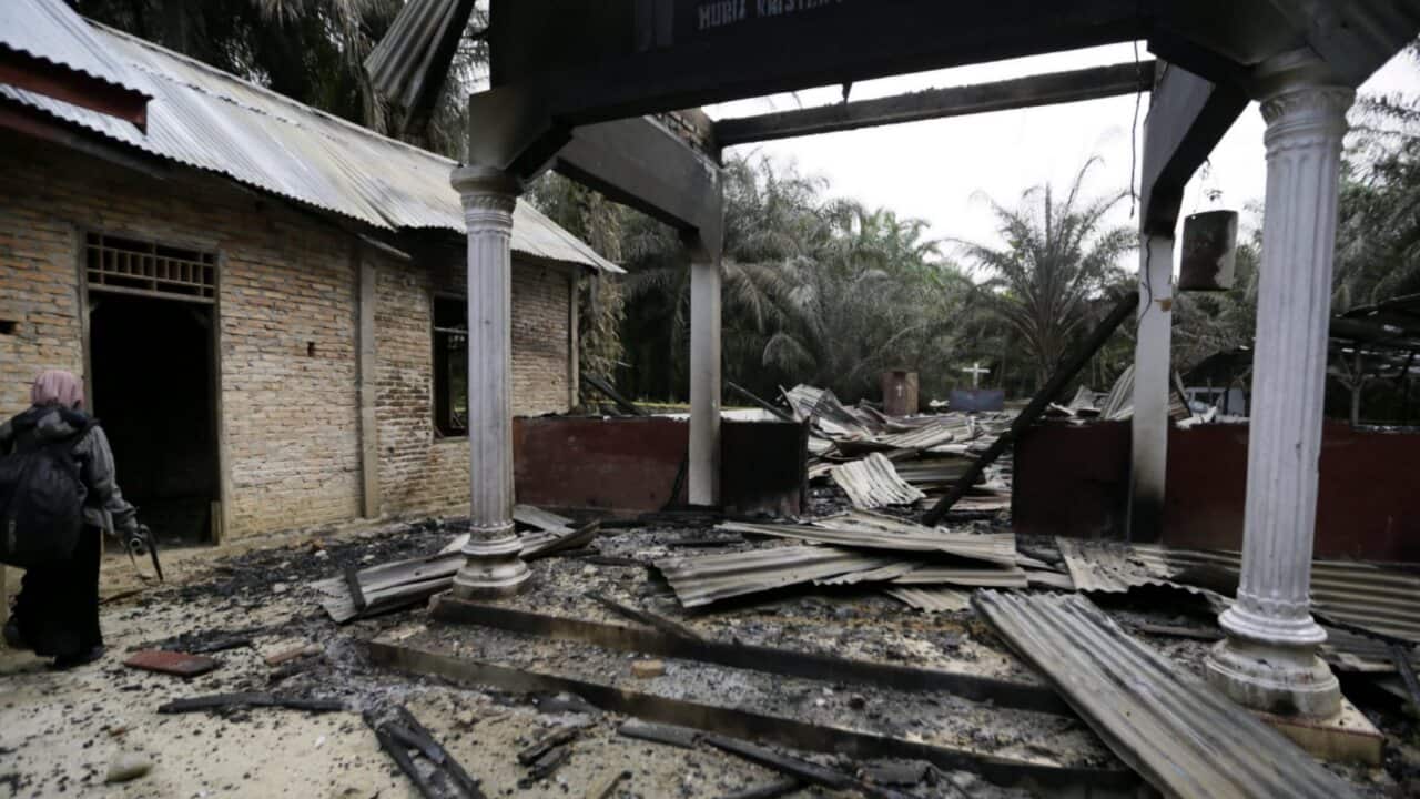 An Acehnese woman walks next to a burned Church in Aceh Singkil, Indonesia
