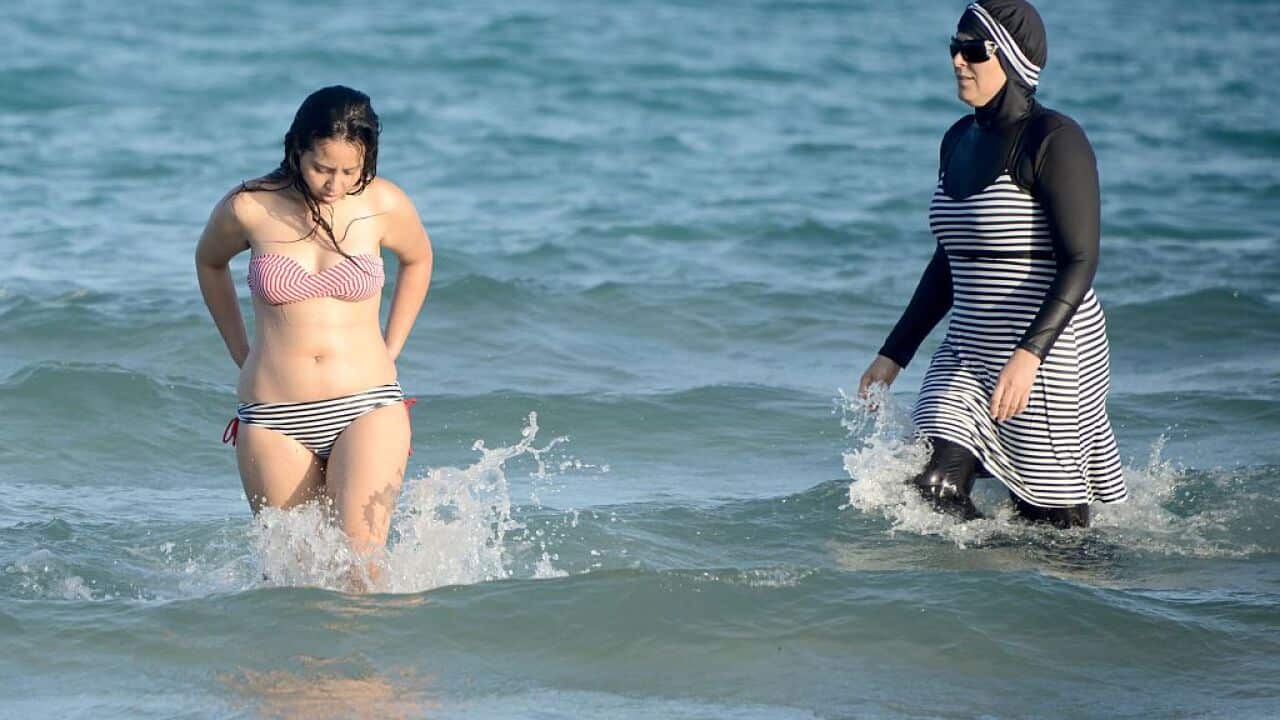 Tunisian women, one (R) wearing a "burkini", a full-body swimsuit designed for Muslim women, swim on August 16, 2016