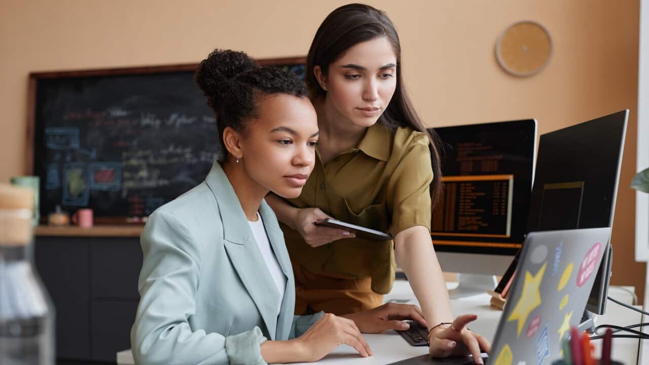 Two young women using laptop together while reviewing code