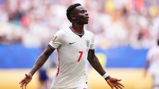 A black football player in a white English jersey celebrates a goal with his arms outstretched
