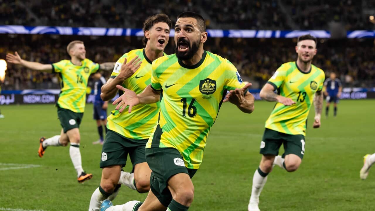 Australian football players in green and gold uniforms celebrate on the pitch.
