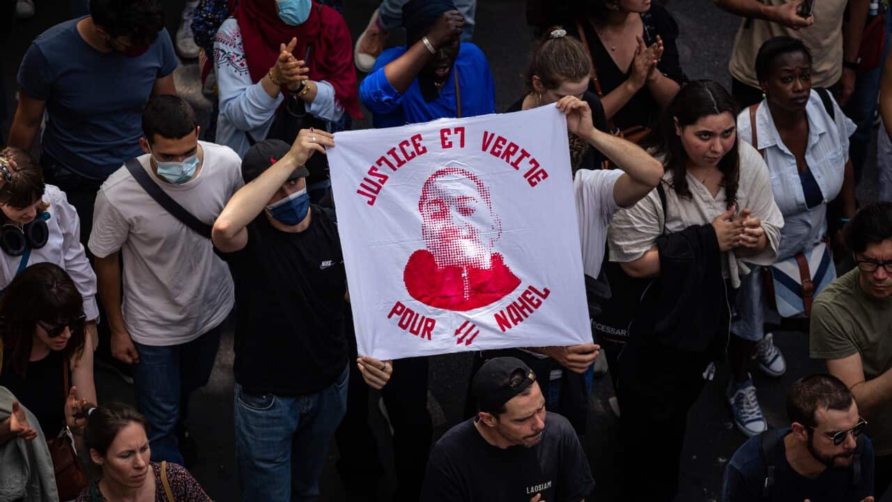 Protesters march with a flag that says "Justice and truth for Nahel"