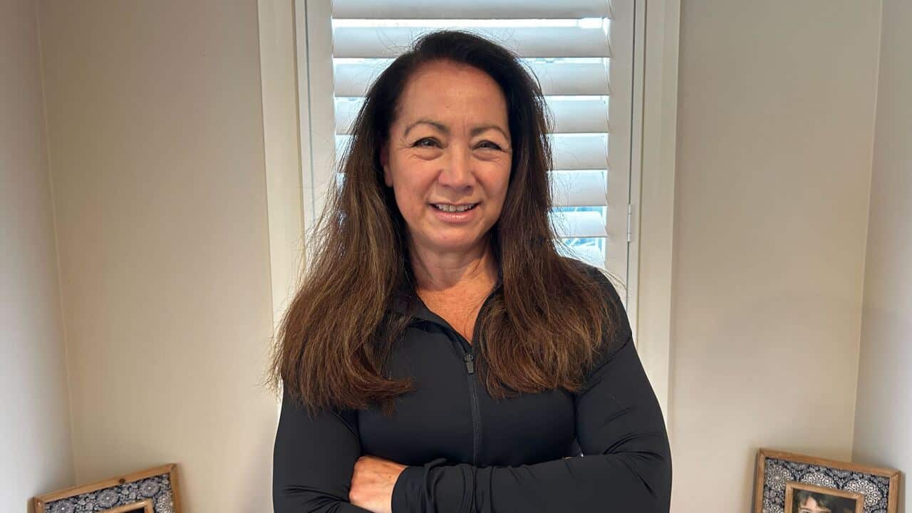 A woman wearing a black jumper standing in front of two photos of children
