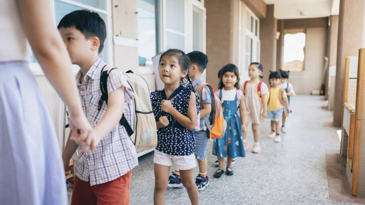 Preschool teacher guiding and arranging students waiting in line entering classroom