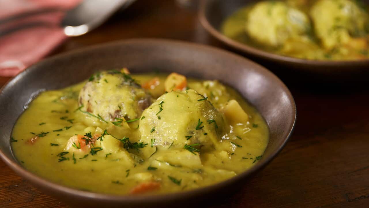 A wide browl bowl with a vibrant yellowish soup sits on a table, with a second bowl of soup behind it.