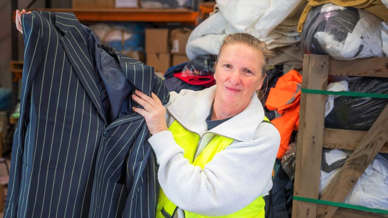 A woman in a hi-viz vest stands holding a striped school uniform blazer in a warehouse.