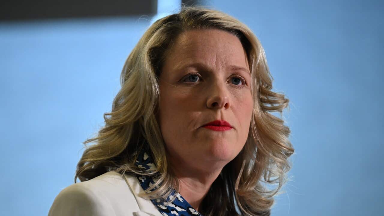 A blonde woman in a white jacket and blue patterned shirt