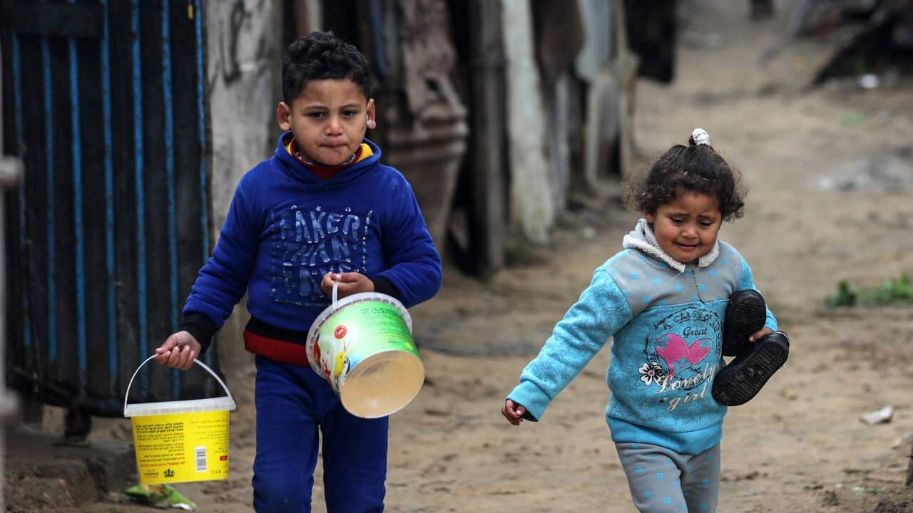Two Palestinian children walk past makeshift shelters holding pots