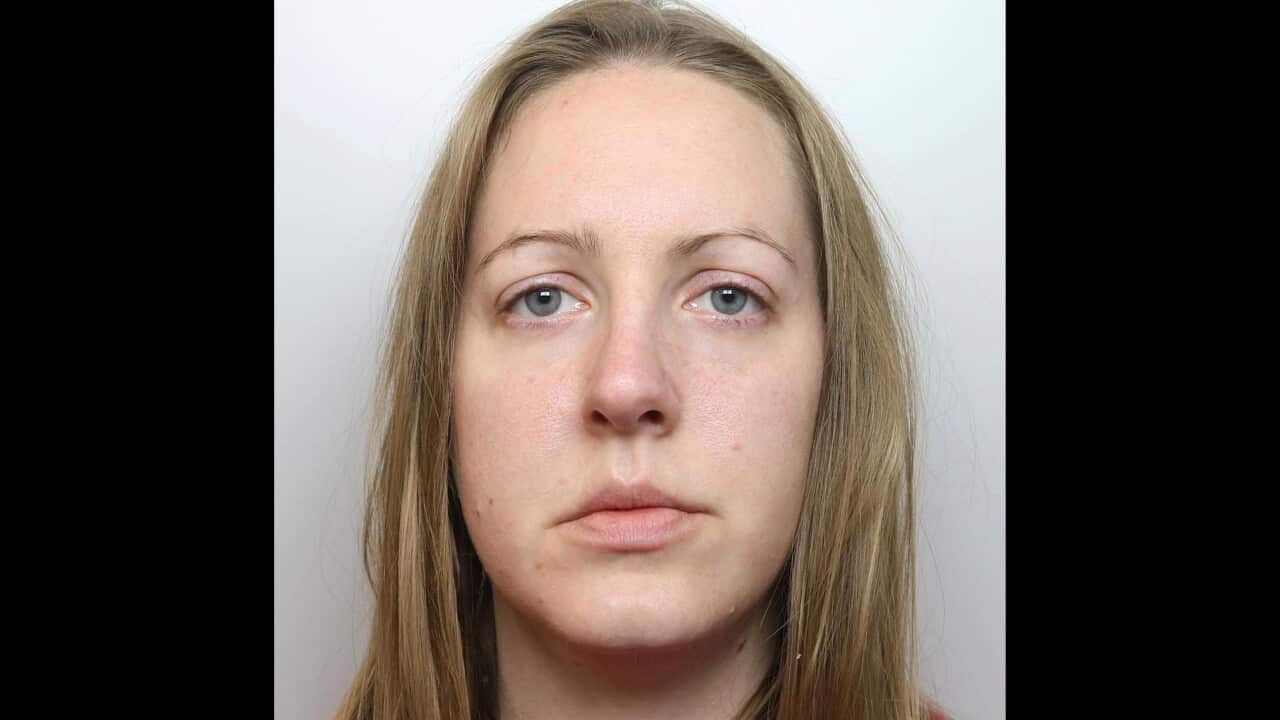 A headshot of a woman with long blonde hair, light-colored eyes, and a neutral expression looking directly forward against a plain light grey background.