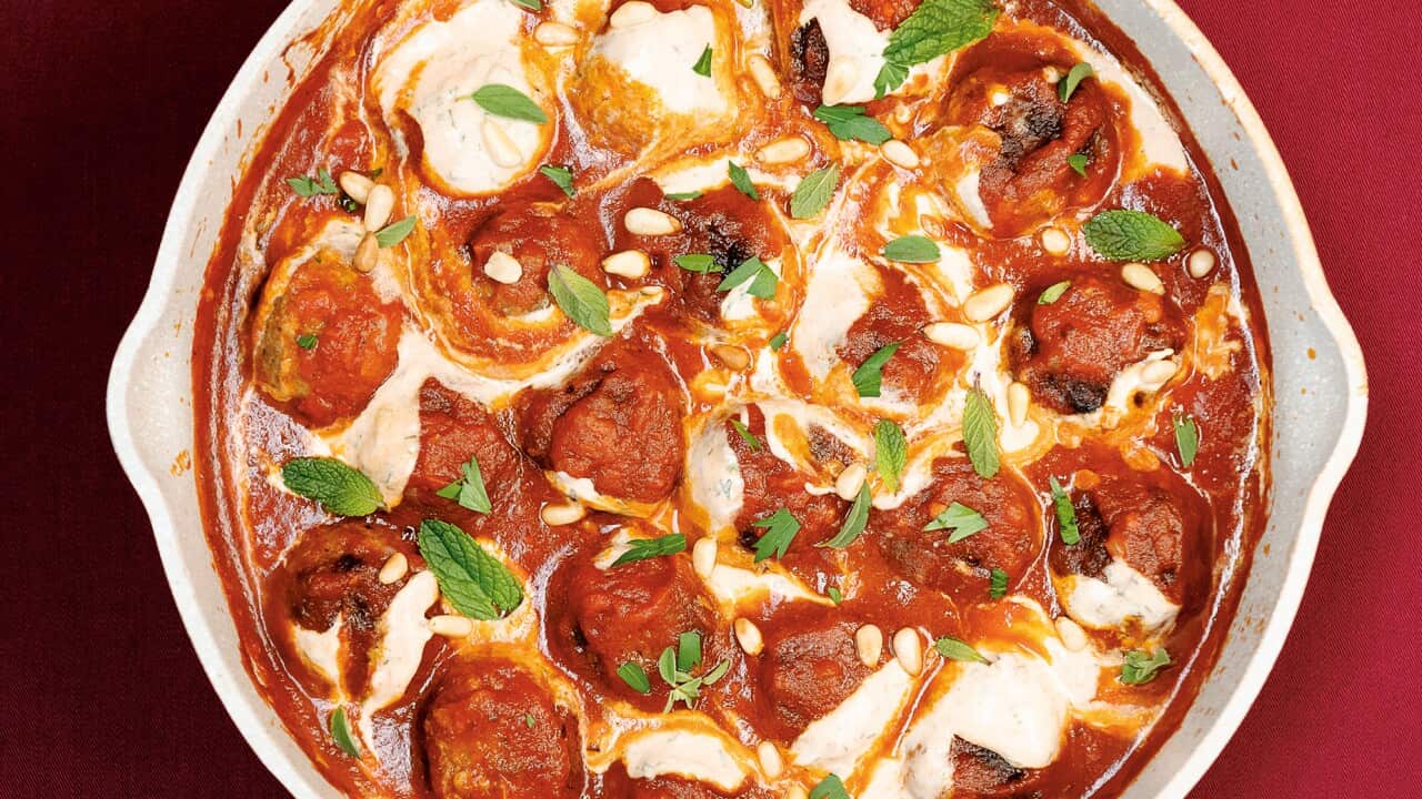 A white cast iron sauce pan holds meatballs in a rich, red sauce, drizzled with yoghurt and scattered with