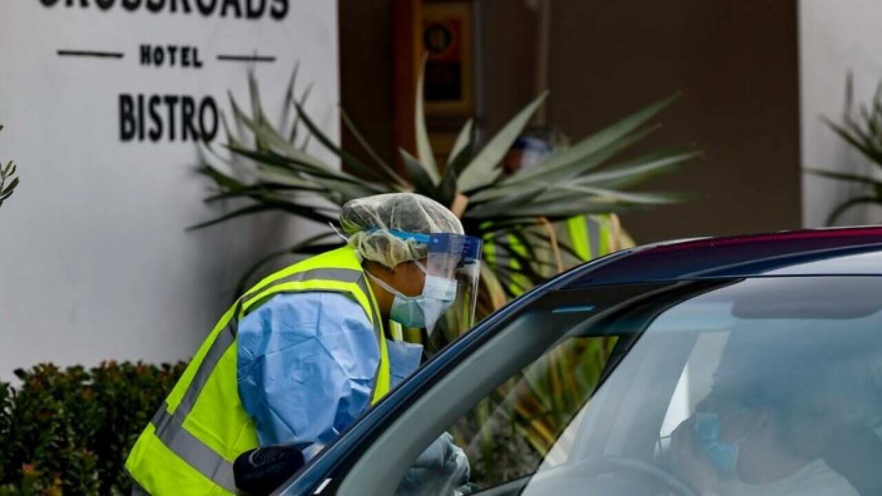 Workers administering COVID-19 tests to people in their cars at the Crossroads Hotel testing centre