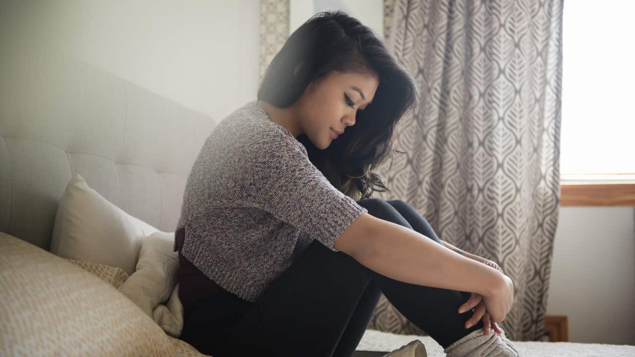 Depressed Mixed Race woman sitting on bed