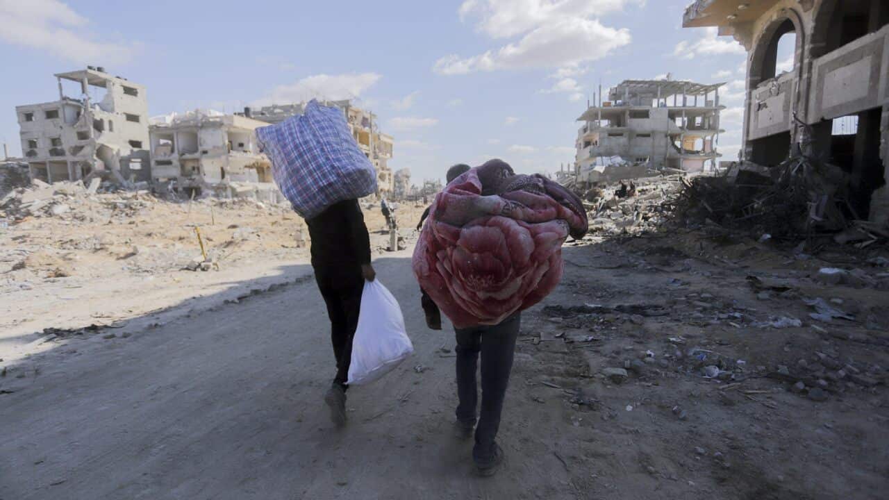 People walking with their belongings surrounded by rubble.