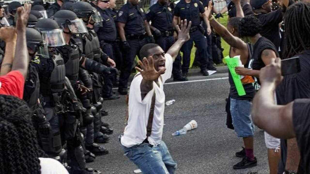 A man attempts to stop protesters from engaging with police in front of the Baton Rouge Police Department headquarters while another man films the protest.