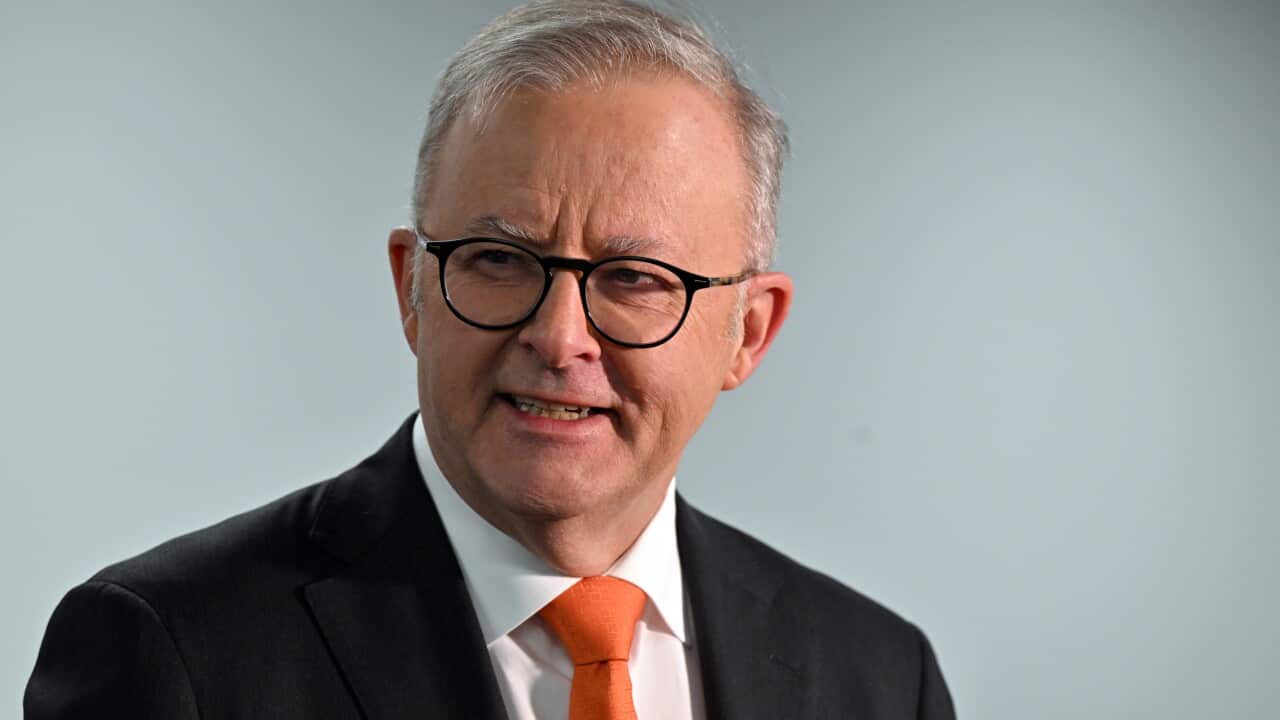 A man wearing a suit, tie and glasses is speaking.