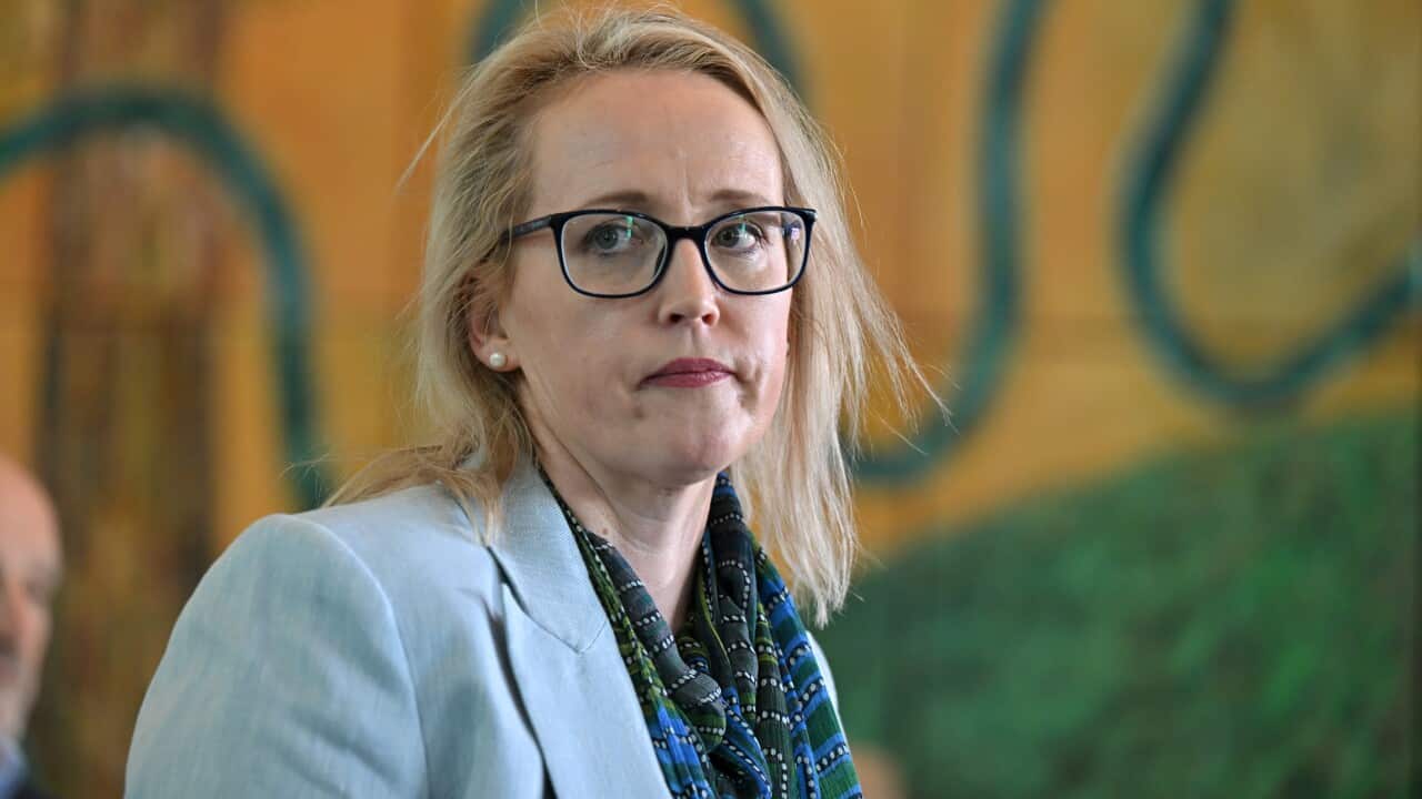 A woman standing inside wearing glasses and a blue blazer.
