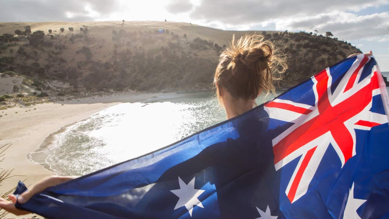 Travel woman stands on cliff above beach holding Australian's flag