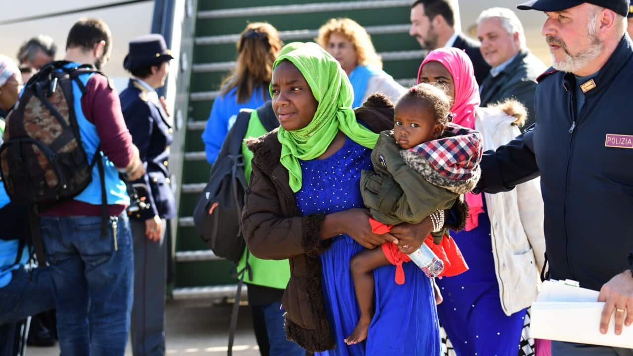 Umuporisi(Iburyo) aherekeje umukenyezi arikumwe n'umwana. polirisi yari yakiriye umurwi w'abimukira 51 bavuye muri Niger kw'itariki 14 Munyonyo 2018.