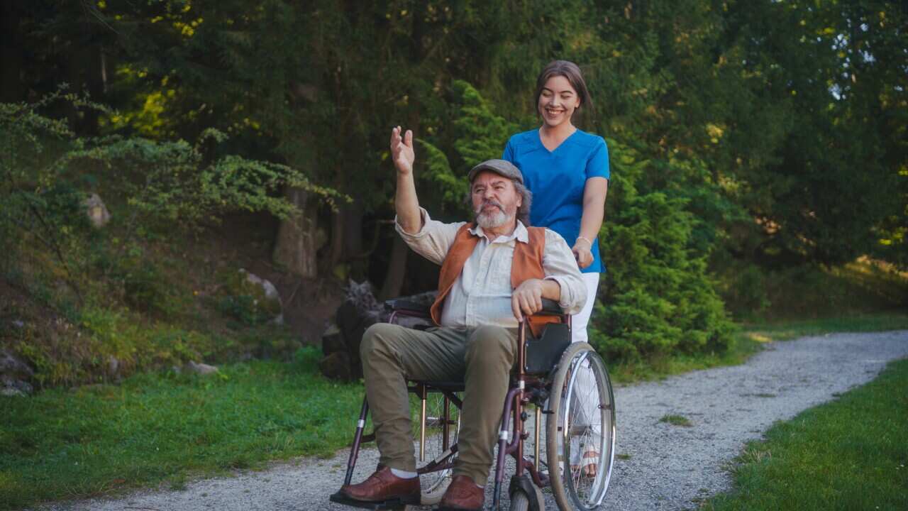 Young caregiver pushing patient on wheelchair from a nursing home in the park.